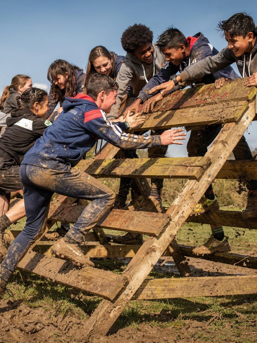 A youth rugby team tackling a muddy assault course together in tracksuits