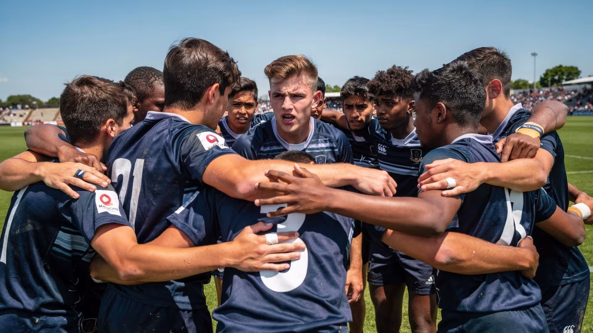 An all-male youth rugby team huddled together with a captain speaking before a match