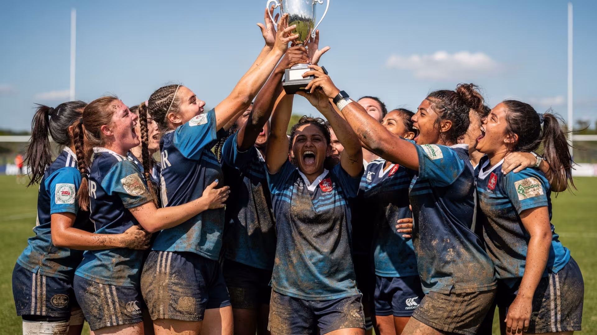 An all-female youth rugby team celebrating and raising a trophy after winning a match