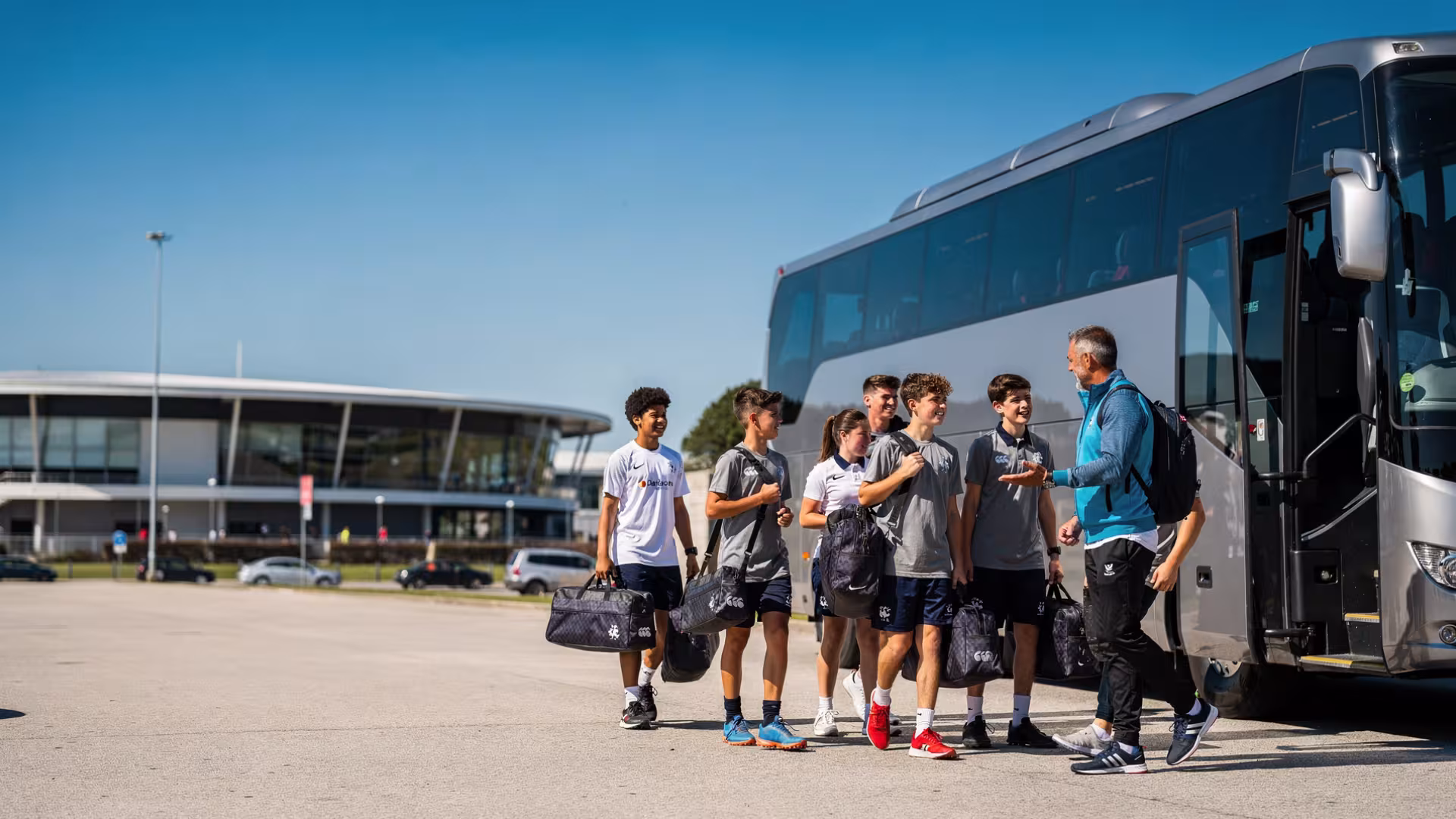 Teenage rugby players and coach arriving beside a team coach