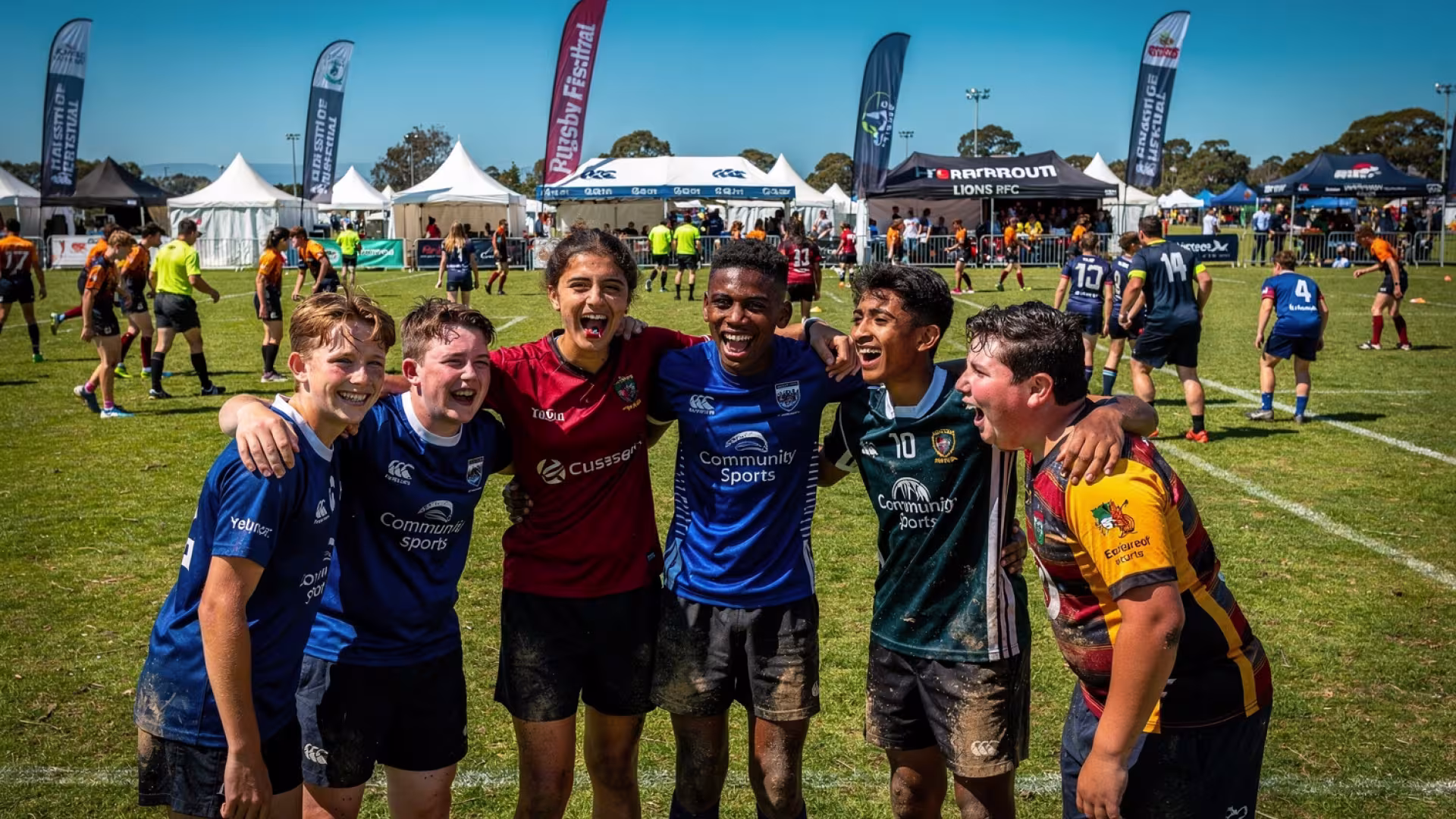 Youth rugby festival players celebrating together pitch-side, festival tents in the background