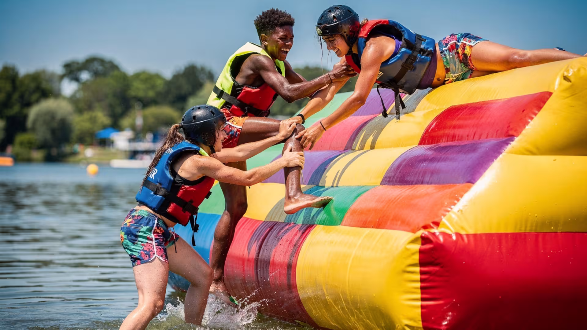 Three teenage teammates working together to climb an inflatable obstacle at a water park