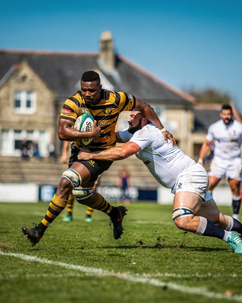 A player being tackled at a European club ground, stone clubhouse in the background