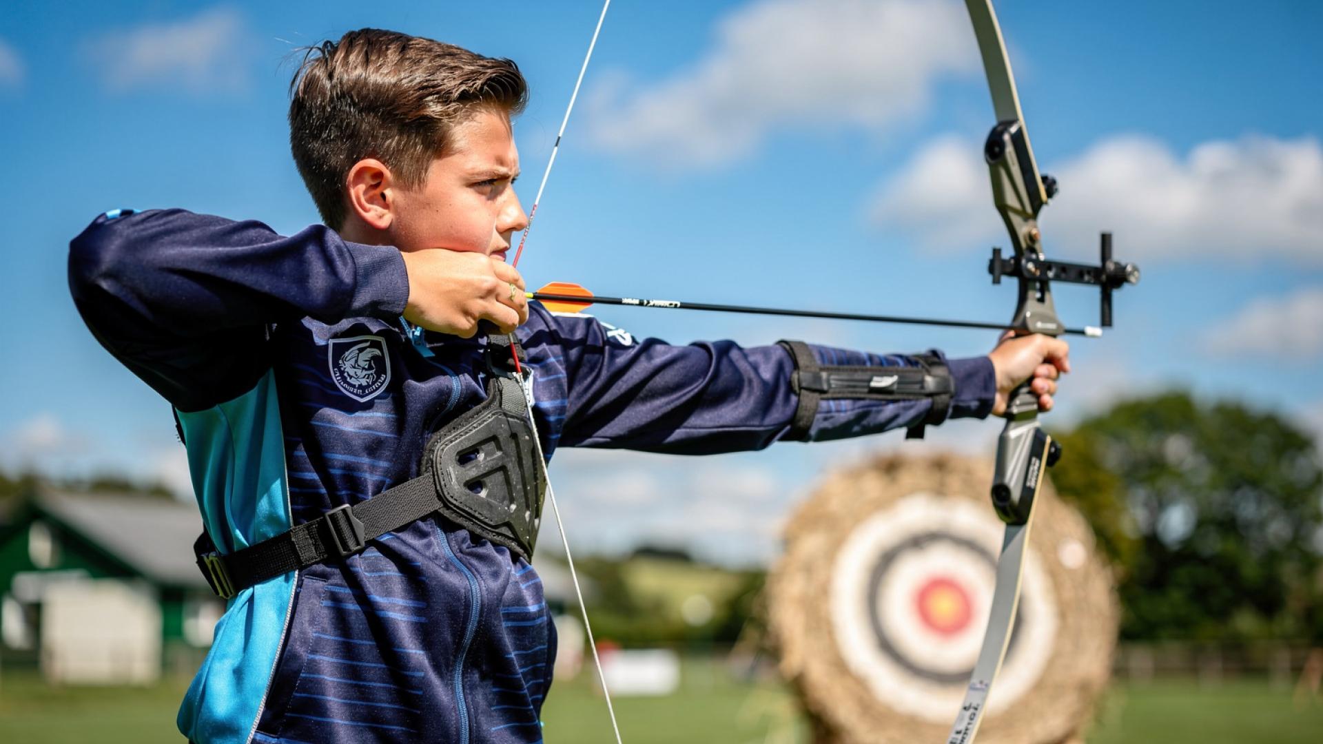 Youth rugby player fully focused, bow drawn during an outdoor archery session